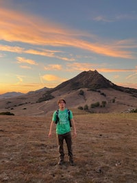 a man standing in a field with a mountain in the background